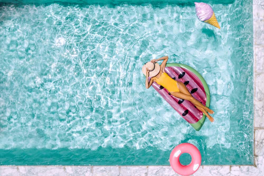 Woman relaxing on watermelon lilo in the pool at private villa. Inflatable ring and mattress. Summer holiday idyllic. High view from above. - Getting Your Pool Ready For Summer