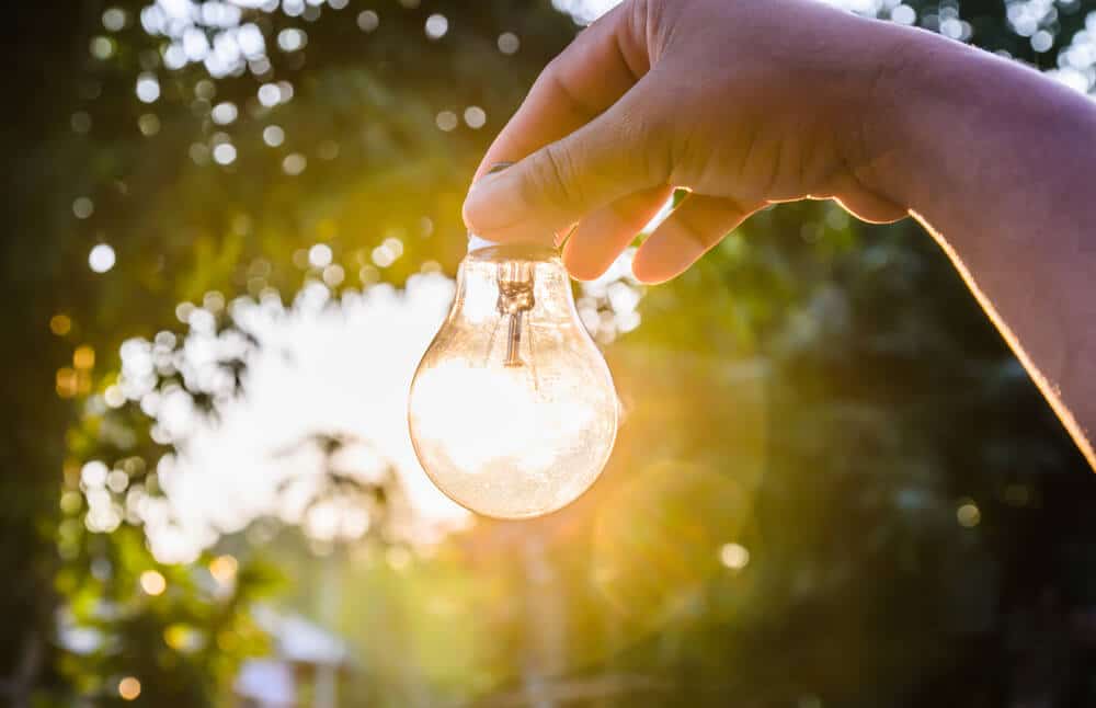 hand holding a light bulb with sunset power concept - How Solar Energy Is Changing Our Relationship with Electricity